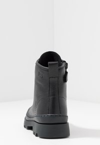 Botte cheville en cuir noir avec surface texturée, bout rond et semelle en caoutchouc robuste. Comprend une languette à l'arrière et une fermeture à glissière.