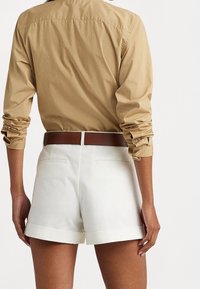 Hnědé tričko s dlouhým rukávem a ohrnutými rukávy, v kombinaci s bílými šortkami s ohrnutým lemem a dvěma zadními kapsami, s hnědým páskem.