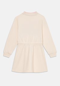 Kremowa sukienka z długim rękawem, z wysokim kołnierzem wykończonym różową lamówką, elastycznym pasem i marszczoną spódnicą. Miękka tkanina i ściągacze przy mankietach.