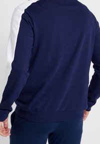 Felpa a maniche lunghe blu navy con accenti bianchi sui lati, polsini e orlo a coste, e texture liscia. Vista posteriore.