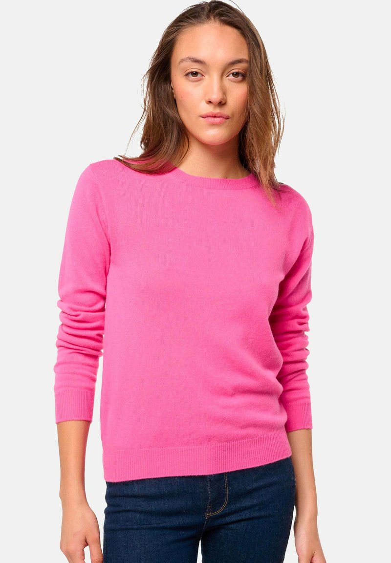 Pull-over rose en tissu doux, avec des manches longues, un col rond et des poignets et un ourlet côtelés. Porté avec un jean foncé.