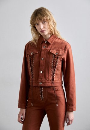 Rust-colored cropped denim jacket featuring metal buttons, front pockets, and lace-up detailing along the sides. Smooth texture.