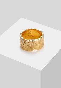 Guld ring med en struktureret overflade og uregelmæssig form. Indskriften indeni lyder "Kuzzoí" og "925", hvilket angiver indholdet af sterling sølv.