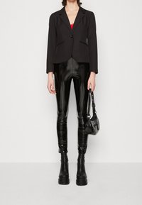 Svart skräddarsydd blazer med en enda knapp, som matchas med högblanka svarta leggings och kraftiga platåstövlar. Liten svart handväska med rem.