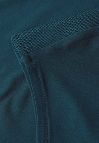 Tissu en mélange de coton de couleur bleu sarcelle foncé avec une texture lisse. Présente un col texturé et côtelé ainsi que des coutures visibles le long des bords.
