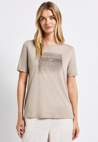 Beige t-paita lyhyillä hihoilla, jossa on neliömäinen graafinen kuva, jossa lukee "GOLDEN HOUR" ja "A GLIMPSE OF SUN" erottuvilla väreillä. Pehmeä kangas, rento leikkaus.