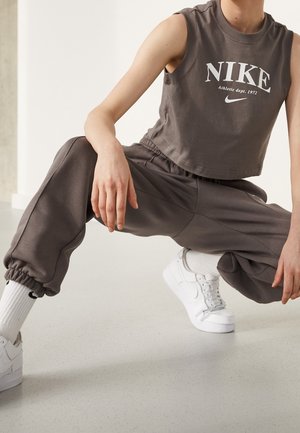 Mørkegrå kort tanktop med hvid "NIKE" logo, parret med matchende løstsiddende joggers og hvide sneakers. Glat stof, elastiske manchetter.