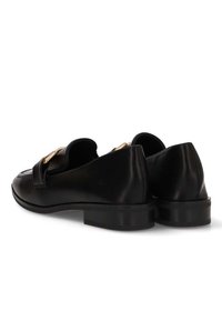 Mocasines de cuero negro con un tacón bajo, punta redonda y herrajes decorativos en tono dorado en la parte delantera. Textura suave, diseño minimalista.