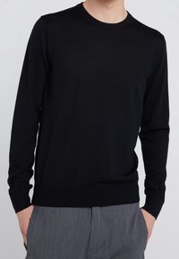 Svart långärmad tröja i lättstickad tyg. Har rund halsringning och ribbade manschetter och nederkant. Slät textur.