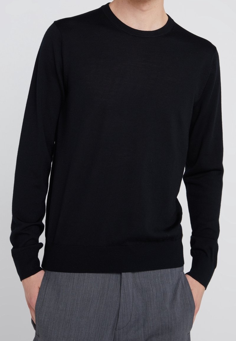 Svart långärmad tröja i lättstickad tyg. Har rund halsringning och ribbade manschetter och nederkant. Slät textur.