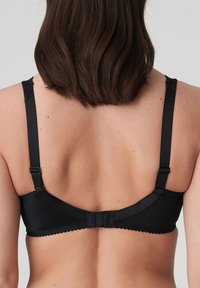 Black bra with adjustable straps, scalloped edging, and a hook-and-eye closure. Made of smooth material, featuring a decorative lace detail at the strap.