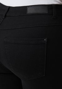 Svarta denimjeans med en elegant design, som har en enda bakficka och en subtil logotyp vid midjan. Slät textur.
