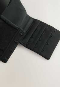 Soutien-gorge taille noir en tissu avec des fermetures à crochets et œillets réglables. Présente une texture lisse avec une section en maille et des détails de couture robustes.