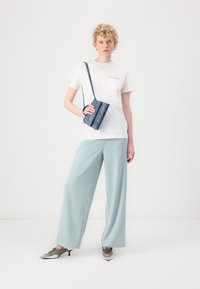 White short-sleeve t-shirt with a chest pocket, paired with light blue wide-leg trousers and silver pointed-toe heels. Small blue bag.