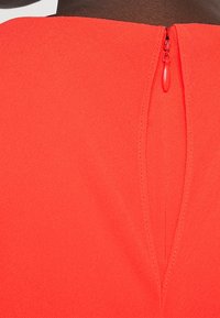 Närbild av ett rött plagg med en delvis dragkedja på ryggen mot mörk hud.