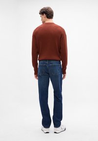 Maglione a coste color ruggine, jeans in denim, sneakers bianche. Focus sul maglione testurizzato, sul colore blu dei jeans e sullo stile di calzature casual.