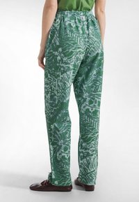 Zielone spodnie w wzory o luźnym kroju, zdobione kwiatowym motywem w jaśniejszym odcieniu zieleni. Wykonane z fakturowanej tkaniny, z elastycznym pasem w talii.