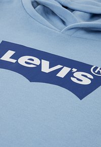Ανοιχτό μπλε φούτερ με απαλό ύφασμα, που φέρει μεγάλο λογότυπο Levi's σε σκούρο μπλε χρώμα με έντονη, λευκή γραμματοσειρά στο μπροστινό μέρος.