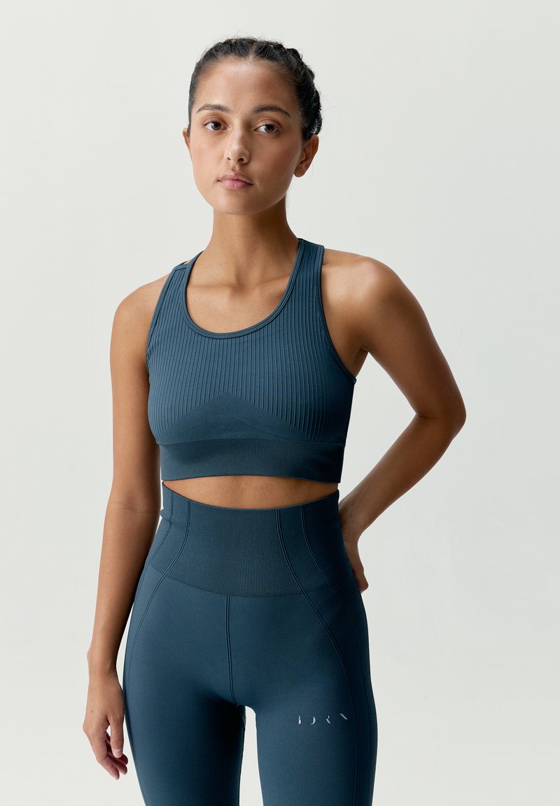 Tmavomodrý športový podprsenka s ribbenou textúrou a úzkym strihom, skombinovaná s legínami s vysokým pásom, ktoré majú podobný ribbený dizajn a jemné akcenty.