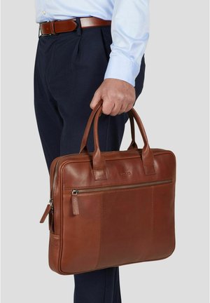 Mann i blå skjorte og mørke bukser som holder en brun skinnmappe med glidelåslomme og to håndtak.