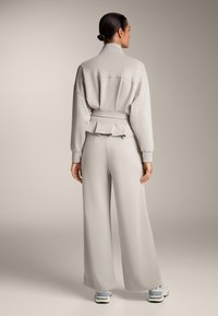 Harmaa verkkaritakki ja leveälahkeiset housut, valmistettu pehmeästä kankaasta. Ominaisuuksiin kuuluu korkea kaulus ja peplum-yksityiskohta vyötäröllä, rento istuvuus.