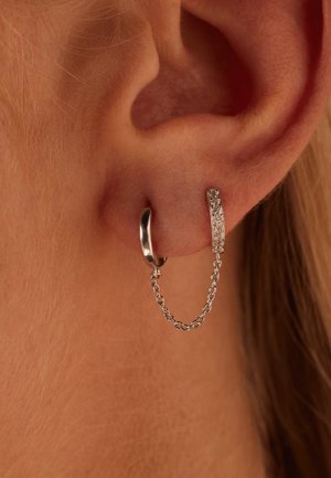 Silberne Creole mit einer Kettenverbindung zu einem geraden, strukturierten, glitzernden Stabstück, das ein modernes, minimalistisches Design zeigt.