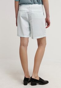 Ljusa mintgröna skräddarsydda shorts av slät tyg, med två bakfickor och raka ben, kombinerade med svarta slip-on skor.