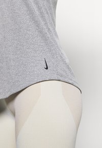 Camiseta deportiva gris de manga corta con un patrón texturizado; logo negro de Nike en el dobladillo. Combinada con mallas de color claro.