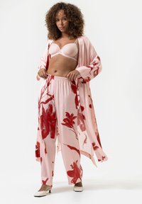 Kimono en satin rose clair avec imprimé floral rouge, associé à un soutien-gorge rose clair et un pantalon assorti avec une taille élastique. Talons blancs.