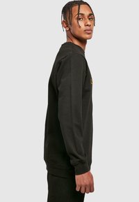 Czarna bluza wykonana z bawełny, z długimi rękawami i okrągłym dekoltem. Na przodzie znajduje się małe żółte logo.