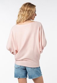 Locker sitzender, hellrosa Pullover mit weitem Ausschnitt und kurzen, voluminösen Ärmeln, kombiniert mit Jeans-Shorts im klassischen Schnitt.