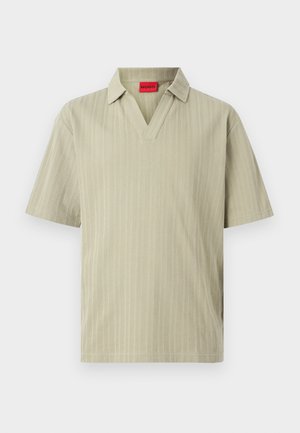 Polo beige clair à manches courtes avec des rayures verticales discrètes et une étiquette rouge "HUGO" à l'intérieur du col.
