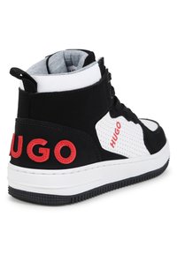 Sneaker alta con materiale perforato bianco e nero, logo rosso "HUGO", lacci neri e suola in gomma bianca con battistrada testurizzato.