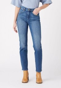 Jeans de tiro alto en azul, fabricados en denim, con una silueta ajustada, diseño de cinco bolsillos y un ligero desvanecimiento. Combinados con botas de tobillo marrones.