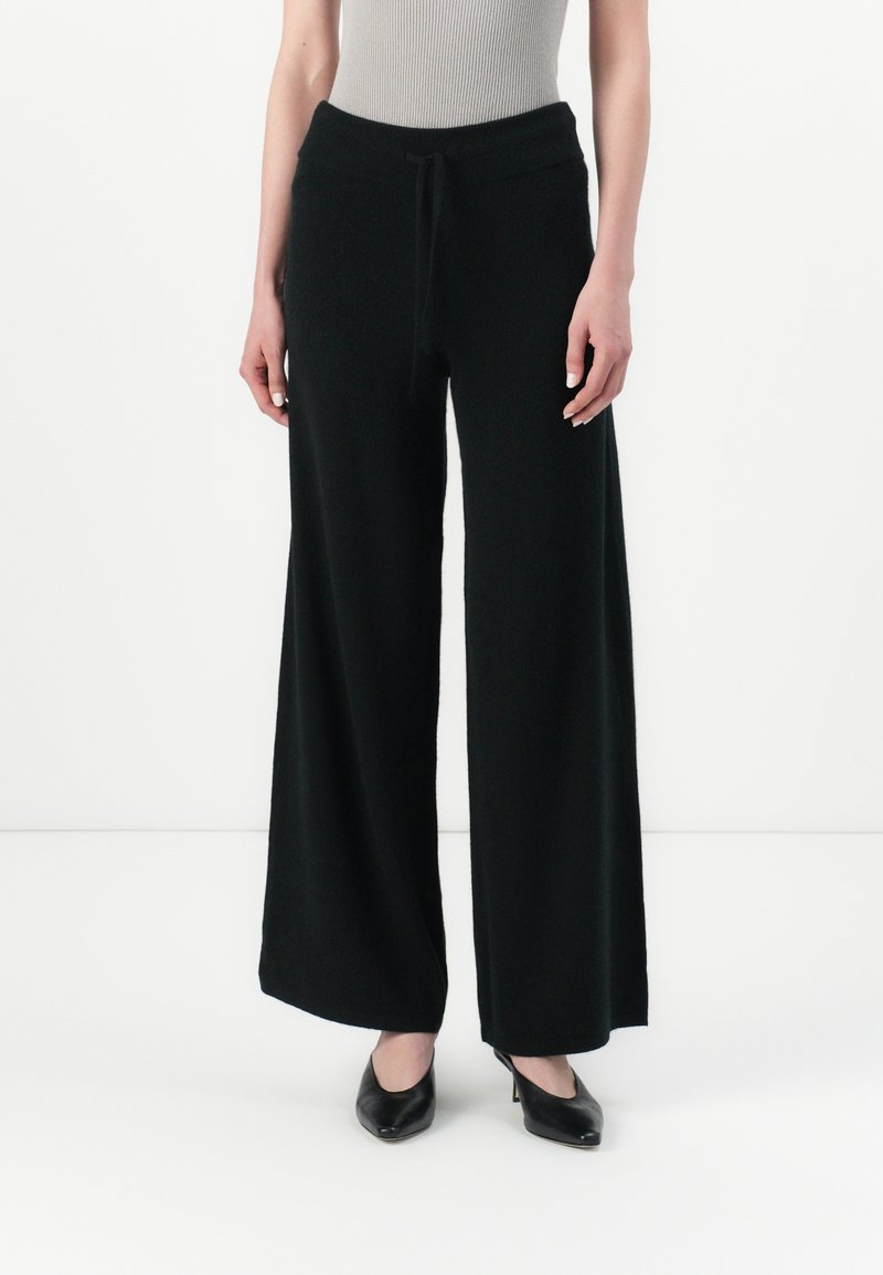 Pantaloni neri a gamba larga realizzati in tessuto morbido, con vita regolabile e vestibilità rilassata, abbinati a tacchi neri.