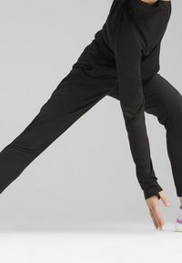 Zwart sportoutfit bestaande uit een top met lange mouwen en taps toelopende broek. Soepele, rekbare stof met minimale naden, ontworpen voor beweging.