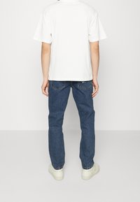 Vit t-shirt med kort ärm, blå denimjeans och vita sneakers. Jeans har bakfickor och uppvikta fållar. Enkel design, avslappnad passform.