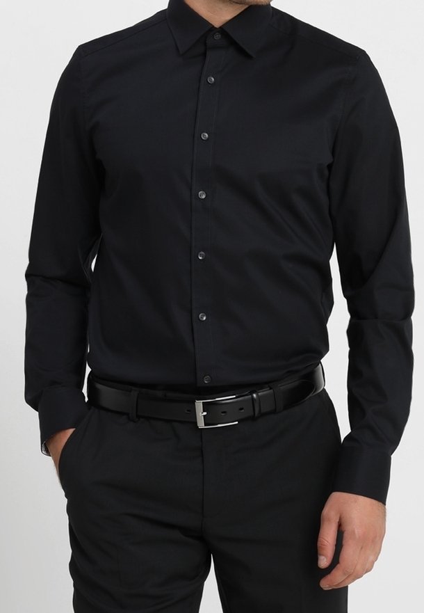 Svart långärmad skjorta med knappkrage, med en mjuk textur och subtil glans, kombinerad med svart bälte och byxor.