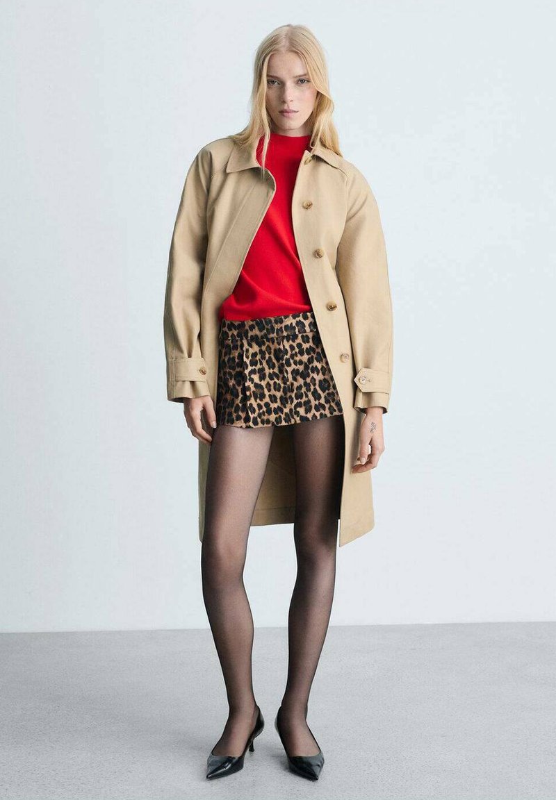 Beige trenchcoat, rode trui, minirok met luipaardprint, zwarte panty en spitse zwarte hakken. Gladde texturen en contrasterende patronen zijn duidelijk zichtbaar.