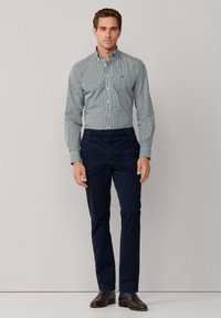 Camisa abotonada con patrón de cuadros en verde y blanco, combinada con pantalones azul marino y zapatos de vestir marrones. Tela suave con ajuste entallado.