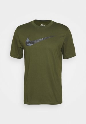 Oliwkowa koszulka Nike z krótkimi rękawami i dużym czarno-szarym kamuflażowym logo Nike Swoosh na piersi.