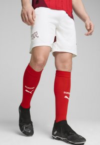 Sarkanais krekls ar horizontālām svītrām, baltās šortos ar logotipu un sarkanas zeķes ar tekstu "SUISSE". Melni futbola apavi ar teksturētu virsmu.