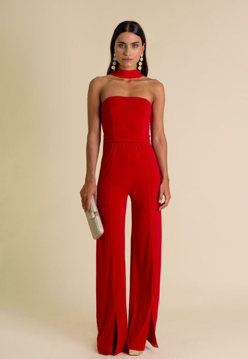 Rode strapless jumpsuit met een aansluitende bovenkant, flare benen, zijsplitten en een zachte textuur. Gecombineerd met een metallic clutch en statement oorbellen.