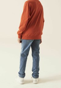 Sudadera naranja, jeans azules y zapatillas blancas. Ajuste casual con puños y cinturilla de canalé. Las zapatillas presentan un logo prominente.