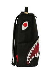Mochila negra con diseño de tiburón, con acentos en blanco y rojo, material texturizado y un patrón de dientes llamativo. Incluye un asa superior y cremallera.