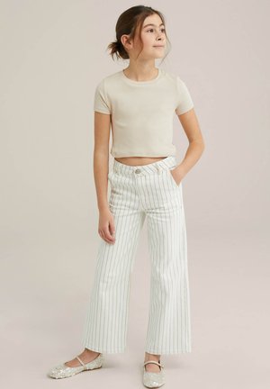 Camiseta corta de canalé crema combinada con pantalones anchos de rayas blancas y zapatos planos brillantes, con un ajuste holgado y detalles sutiles.