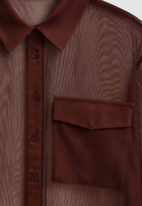 Camicia button-up trasparente marrone con colletto, dotata di taschino e texture liscia. I bottoni sono marrone scuro, in abbinamento al tessuto.