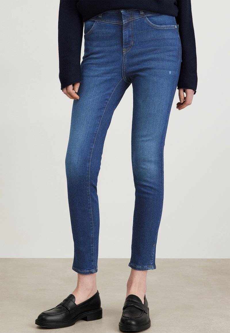 Jeans skinny in denim blu con vita alta e cinque tasche, caratterizzati da una texture liscia e una leggera elasticità per il comfort.