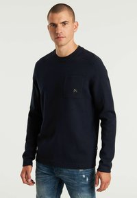 Maglione a maniche lunghe blu navy con scollatura rotonda e tasca sul petto, caratterizzato da polsini a coste e un tessuto testurizzato. Dettaglio del logo discreto sulla tasca.