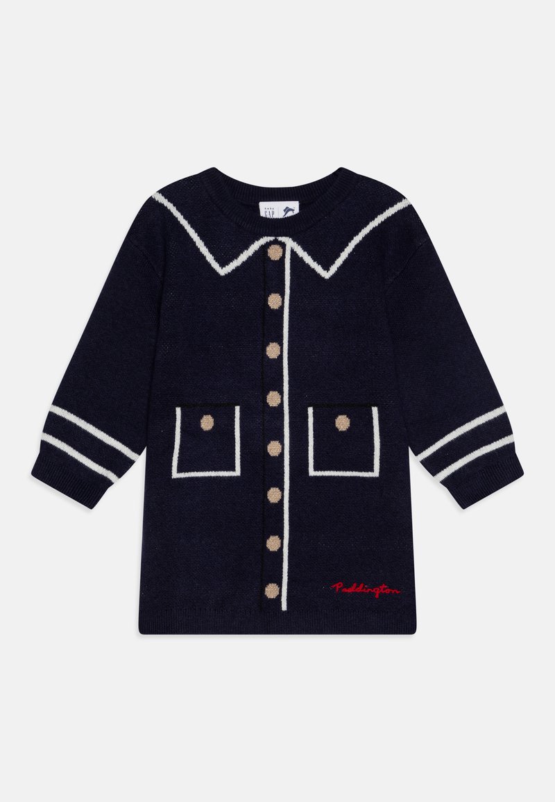 Marineblå strikket kjole med hvit krage og stripete mansjetter. Har dekorative knapper og to frontlommer med beige prikker. Rødt "Paddington" broderi.